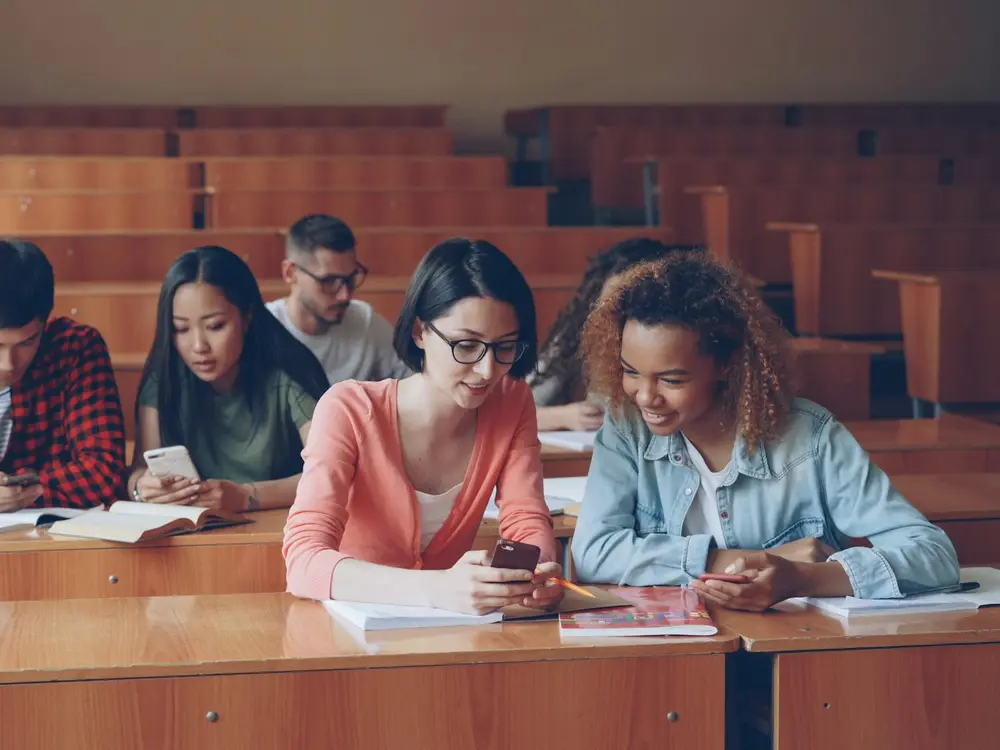 Alunas conversando e olhando o celular em uma sala de aula